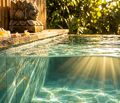 ShuangOu green mosaic pool tiles seen through clear water in a tropical pool with stone coping and frangipani flowers