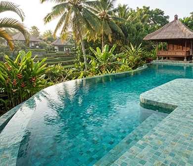 ShuangOu aqua mosaic pool tiles in a curved resort infinity pool surrounded by tropical greenery and thatched pavilions